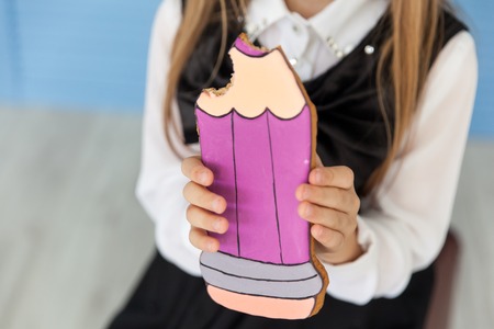 Portrait of a happy school girl in a uniform with big violet gingerbread-pencil. Back to school
