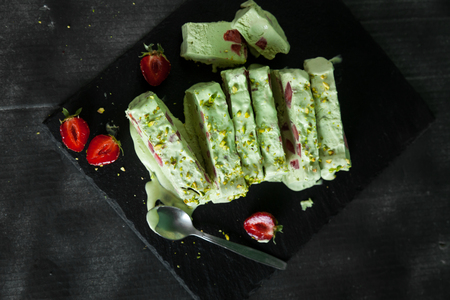Pistachio ice cream with strawberry and pistachio nuts on a black stone backgroundの写真素材