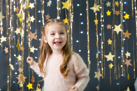 Magic christmas card with a happy girl in a studio with a gold stars garland, fluffy clouds and lights. Happy girlの写真素材