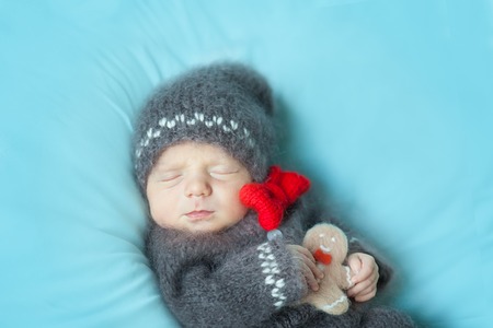 Sleeping newborn baby wearing a crocheted gingerbread man costume with gingerbread cookie plush felt...