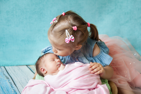 Beautiful blond girl hugging her sleeping newborn sister, beautiful sistersの写真素材