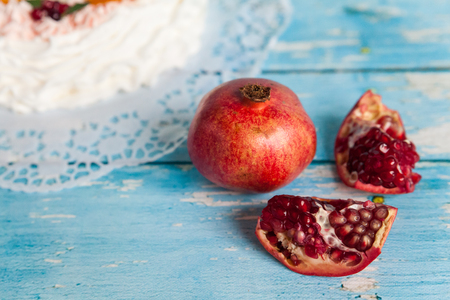 Ripe pomegranate slices near pavlova cake wreath on blue wooden background with pomegranate seedsの写真素材