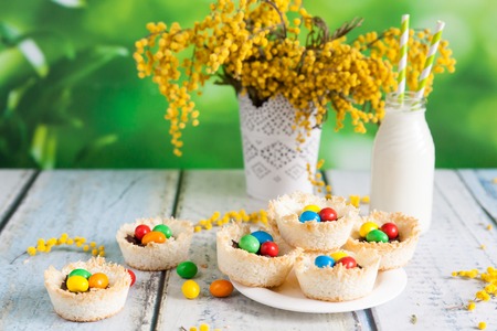 Springtime coconut birds nests filled with Easter eggs on a wooden background. Laced vase with a...