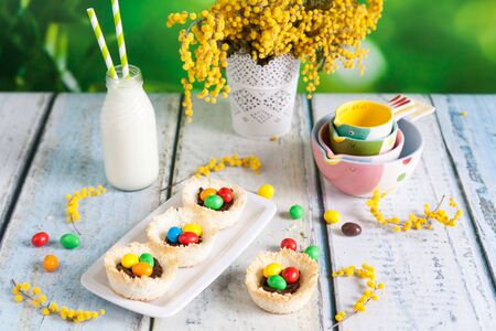 Springtime coconut birds nests filled with Easter eggs on a wooden background. Laced vase with a...