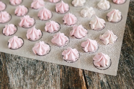 Small white and pink meringues or zephyr on a silicone mat on wooden backgroundの写真素材