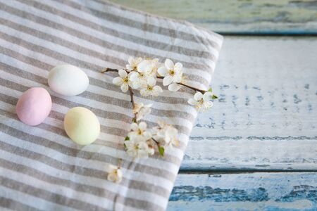 Table-napkin and blooming cherry branch on a wooden background. Easter decor with pastel chocolate...
