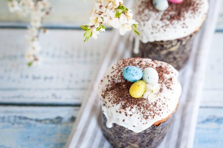 Easter cake kulich. Traditional Easter sweet bread decorated with sugar glaze and candy cane shape eggs and chocolate chips. Easter orthodox cake and cherry blossom twig in the backgroundの写真素材