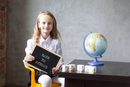 School girl in a uniform holds a blackboard. back to school concept. Distance learning from home