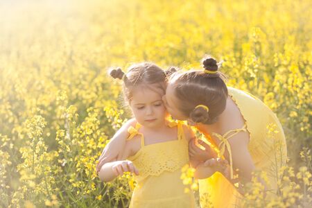 Cute girls in yellow dresses having fun in the field of flowering rape. Nature blooms rape seed field. Summer holidaysの写真素材