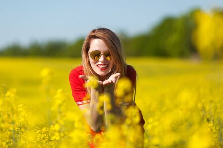 Happy young woman in a red dress enjoying summer in the rape field