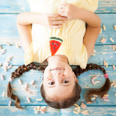 Funny little girl with sprinkled lips and freckles upside down on color background with colorful...