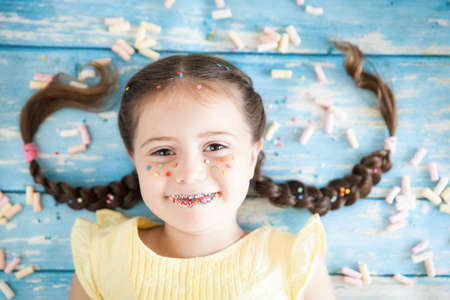 Funny little girl with sprinkled lips and freckles on color background with colorful candies. Happy childhood conceptの写真素材