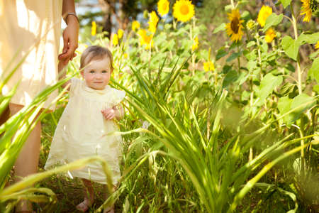 Cute baby girl in a yellow dress having fun on a sunflower summer fieldの写真素材