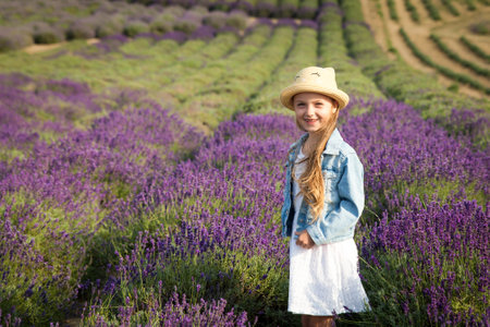 Cute little girl in a white dress and jean jacket having fun in a lavender fieldの写真素材