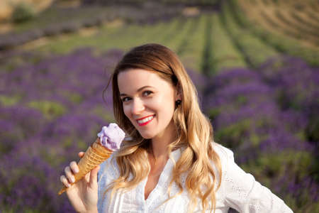 Young woman in a white dress eating lavender ice-cream in a lavender fieldの写真素材