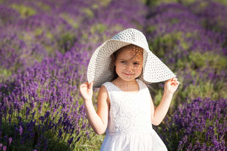 Cute little girl in a white dress and big hat having fun in a lavender fieldの写真素材