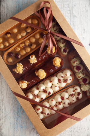 Set of eclair cakes and tartletes with different fillings in a box. Chocolate, caramel, pistachio,...