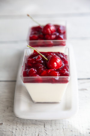 Creamy panna cotta with cherry sauce in glass jars on a light wooden background. Italian Desserts without baking. Valentine's Dayの写真素材