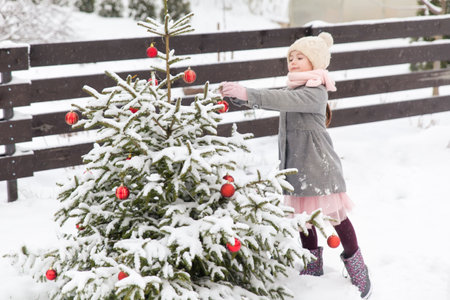Girl playing near the decorated Christmas tree in a winter gardenの写真素材