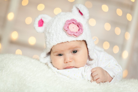Cute adorable child with warm white and pink bear hat. Happy girl on white background with lights...