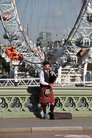 London, Great Britain - October 10, 2012: Bagpipe player on Westminster Bridge in front if the London Eyeのeditorial素材