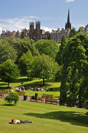 Edingburgh, Scotland - July 7, 2010: Princess Street Gardens in Edinburgh/Scotland with view to the historic city center and the church of scotland assembly hall. In the front is a man relaxing in park and another talking to a group of students.のeditorial素材