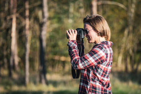 Young female photographer taking a photo outdoors in the woods in warm eventing light