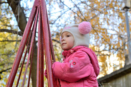 baby girl in a pink hat and red jacket playing in the playground. Late autumn urban playgroundの写真素材