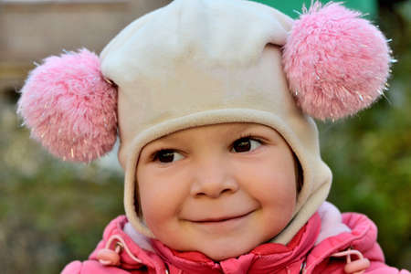 close-up portrait of a smiling baby girl in a pink hat with pom-pomsの写真素材