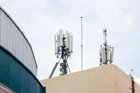 Cell site Post / transmitters on the roof top of white building with office building as background.の写真素材