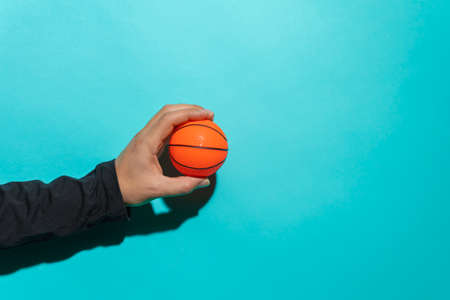 Hand holding a small basketball in front of colorful blue background with copy space for text.の写真素材