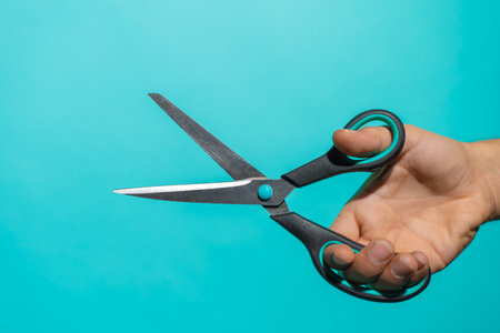 Hand with colorful pair of scissors in front of a blue background with copy space for text and designs.の写真素材