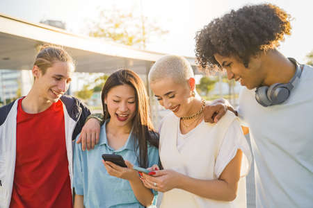 Multiracial happy teenage friends looking the phone and laughing in the campus.