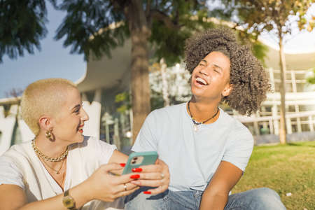 Afroamerican and caucasian couple laughing, looking the phone and listening to music in the city.の写真素材