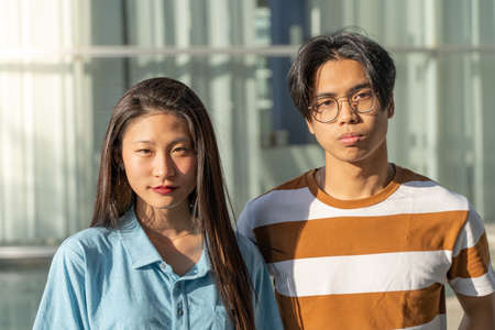Portrait of a beautiful asian couple looking at camera outdoors in the student campus during a sunny...