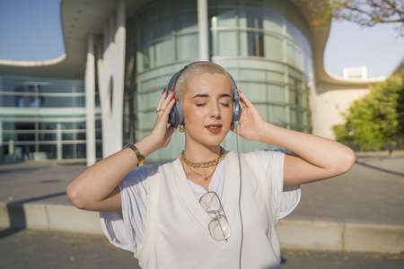 Young beautiful girl with short white hair happy and dancing in the street with headphones.