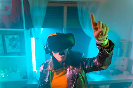 Wireless technologies. Young woman using virtual reality glasses in the dark room with neon...