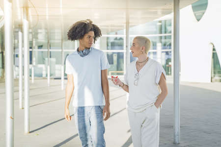 Multiethnic young couple walking and talking happy on the modern university campus during a sunny day.の写真素材