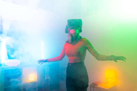 Young woman using virtual reality glasses in the dark room with neon lighting. Wireless...