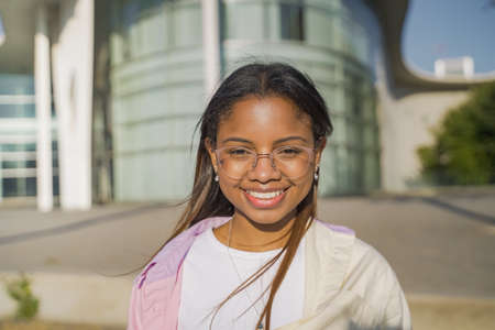 Portrait of a beautiful latin woman smiling and looking at camera outdoors in the student campus during a sunny day.の写真素材