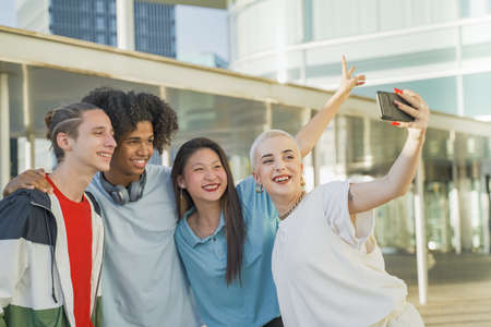 Multiethnic teenage friends taking a selfie group photo and laughing happy in the campus. Technology...