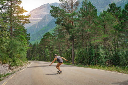 Hipster guy with long board with open arms enjoying life in the middle of a mountain road and a beautiful landscape.の写真素材