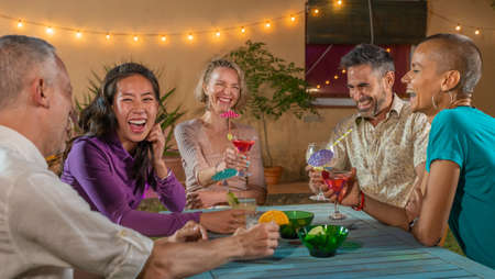 Cheerful friends drinking cocktails. Mature people having fun summer night. Lifestyle and nightlife...