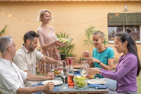 Mature happy friends dining together in barbecue dinner party in summer. Smiles, cheerfulness...
