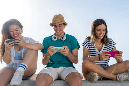 Multicultural group of trendy young friends having fun using smartphones and social media. Mobile...