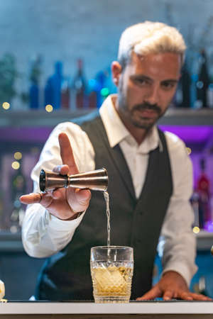 Barman making cocktail in night club adding ingredients and creating expert drinks on bar counter.