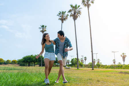 Happy friends walking laughing and holding each other in beautiful park with palm trees.の写真素材