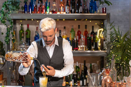 Elegant barman making cocktail Mojito in night club adding ingredients and creating expert drinks on bar counter.の写真素材