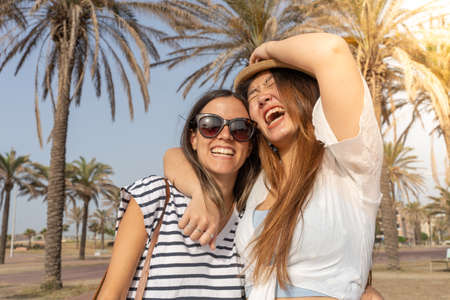 Happy friends laughing and holding each other in the beach. Cheerful girls embracing each other.