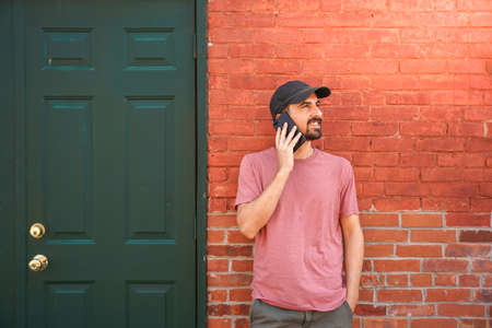 Young man talking with smartphone in front of a brick wall building in the city.の写真素材